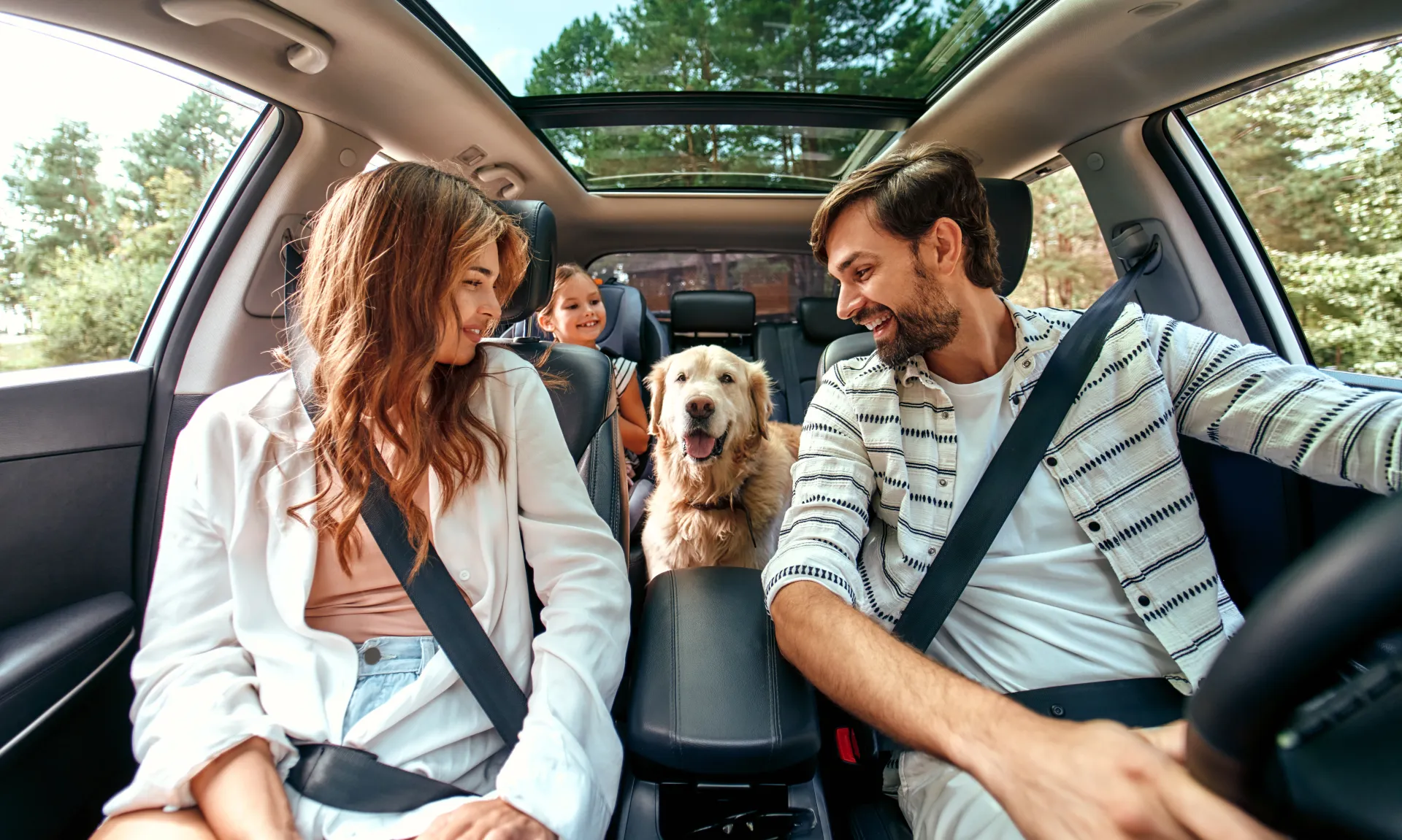 The whole family is driving for the weekend. Mom and Dad with their daughter and a Labrador dog are sitting in the car.
